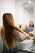 © Zoran Jesic - Woman brushing long brown hair in bathroom mirror reflection