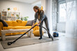 © Zoran Jesic - Woman vacuuming living room rug for home cleaning chores