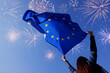 © New Africa - Woman holding flag of European Union against colorful fireworks in sky