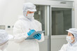 © buritora - Male and female staff working in a manufacturing factory wearing protective clothing and clean wear