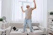 © SHOTPRIME STUDIO - Happy man celebrating work-life balance while standing on the couch in a cozy home office environment, reflecting modern challenges and self-care.