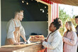 © Seventyfour - Caucasian young adult man serving Black young adult woman at outdoor food stand, Caucasian young woman and Caucasian young man waiting in line behind her