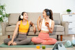 © Nuttapong punna - Two women enjoying home workout on yoga mat with headphones and mobile devices. Healthy lifestyle, fitness, wellness