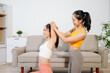 © Nuttapong punna - Personal trainer assisting woman with yoga workout at home. Indoor fitness training, stretching and wellness lifestyle with online guidance and healthy routine.