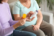 © Pixel-Shot - Young nurse giving pills to senior woman on sofa at home, closeup