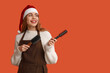 © Pixel-Shot - Young female hairdresser in Santa hat with brushes pointing at something on red background