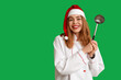 © Pixel-Shot - Portrait of young female chef in Santa hat with ladle on green background