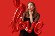 © Pixel-Shot - Young woman with word LOVE made of balloons blowing kiss on red background. Valentine's Day celebration
