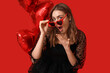 © Pixel-Shot - Surprised young woman in heart-shaped sunglasses and balloons on red background. Valentine's Day celebration