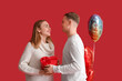 © Pixel-Shot - Lovely couple with gift box and heart-shaped balloons on red background. Valentine's Day celebration