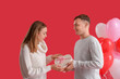 © Pixel-Shot - Lovely couple with gift box and heart-shaped balloons on red background. Valentine's Day celebration
