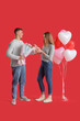 © Pixel-Shot - Lovely couple with bouquet of flowers and heart-shaped balloons on red background. Valentine's Day celebration