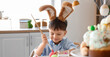 © Pixel-Shot - Cute little boy with bunny ears painting Easter egg at table in kitchen