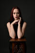 © faestock - close up portrait of beautiful female model with long red hair and black shirt, gestural hand and arm poses, leaning on wooden plinth. classic studio portrait on dark background.