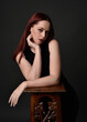 © faestock - close up portrait of beautiful female model with long red hair and black shirt, gestural hand and arm poses, leaning on wooden plinth. classic studio portrait on dark background.