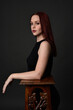 © faestock - close up portrait of beautiful female model with long red hair and black shirt, gestural hand and arm poses, leaning on wooden plinth. classic studio portrait on dark background.
