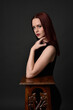 © faestock - close up portrait of beautiful female model with long red hair and black shirt, gestural hand and arm poses, leaning on wooden plinth. classic studio portrait on dark background.