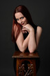 © faestock - close up portrait of beautiful female model with long red hair and black shirt, gestural hand and arm poses, leaning on wooden plinth. classic studio portrait on dark background.