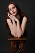 © faestock - close up portrait of beautiful female model with long red hair and black shirt, gestural hand and arm poses, leaning on wooden plinth. classic studio portrait on dark background.