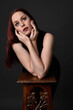 © faestock - close up portrait of beautiful female model with long red hair and black shirt, gestural hand and arm poses, leaning on wooden plinth. classic studio portrait on dark background.