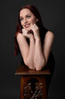 © faestock - close up portrait of beautiful female model with long red hair and black shirt, gestural hand and arm poses, leaning on wooden plinth. classic studio portrait on dark background.