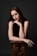 © faestock - close up portrait of beautiful female model with long red hair and black shirt, gestural hand and arm poses, leaning on wooden plinth. classic studio portrait on dark background.