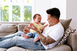 © NZstockphoto - Asian father holding baby girl while seated on the couch