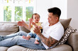 © NZstockphoto - Asian father and baby girl clapping while seated on the couch