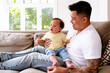 © NZstockphoto - Asian father holding baby girl while seated on the couch
