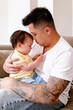 © NZstockphoto - Asian father holding baby girl while seated on the couch