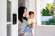 © NZstockphoto - Asian mum standing in porch doorway carrying baby daughter