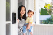 © NZstockphoto - Asian mum standing in porch doorway carrying baby daughter
