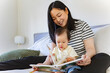 © NZstockphoto - Asian mum reading a book to toddler daughter in bed