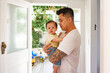 © NZstockphoto - Asian father standing in the doorway holding baby girl