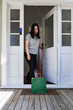 © NZstockphoto - Asian woman opening the door to picking up a package in green paper bag left at the doorstep