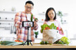 © sofiko14 - A couple is filming a cooking vlog in their kitchen, showcasing fresh produce and healthy eating habits