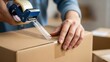 © siam - Hands taping cardboard box with packing tape dispenser background