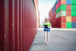 © Wanwajee - Female logistics staff wearing helmet and safety vest adjusting hard hat while standing in container yard. Industrial worker leader, supply chain management, workplace safety focus.