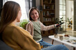 © pressmaster - Caucasian child girl smiling while holding remote control and sitting on sofa with Caucasian woman in living room, engaging in conversation with snacks and drinks on table