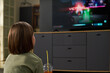 © pressmaster - Caucasian child sitting in living room holding plastic cup with straw watching television screen displaying video game victory message, short brown hair visible from behind