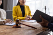 © Wasan - Lawyer holding a law book and explaining legal advice to two businesswoman sitting at a wooden table, during a meeting in the office.
