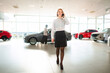 © Jelena - Businesswoman talking on phone walking in car dealership showroom