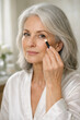 © thodonal - Mature woman applying makeup in soft lighting at home