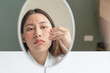 © Pormezz - Asian young woman looking face skin in the mirror have a red rash on her face from cosmetic allergy