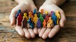 © Yuliia - Protective hands holding diverse colorful paper people figures representing community support, inclusion, teamwork and social unity concepts.