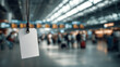 © AnastasiiaAkh - Blank luggage tag hanging in airport terminal with travelers in background, travel concept