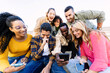 © Xavier Lorenzo - Multiracial group of young students enjoying funny content on a smartphone while relaxing together outdoors. Youth community and friendship lifestyle.