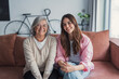 © Daniel - Mother and daughter sit close on a couch at home, hugging and smiling for the camera, capturing a tender family portrait that reflects trust, affection, and a strong bond between two generations