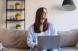 © Daniel - A young woman sits on the sofa at home, looking out the window while reflecting on her work and daily life, showing concentration and a calm freelancer mindset