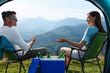 © New Africa - Couple and cool box with bottles of beer in mountains, view from tent